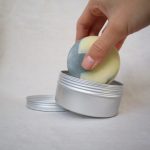 hand placing a big round soap into big round soap tin