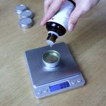 adding essential oil into balm tin on a scale